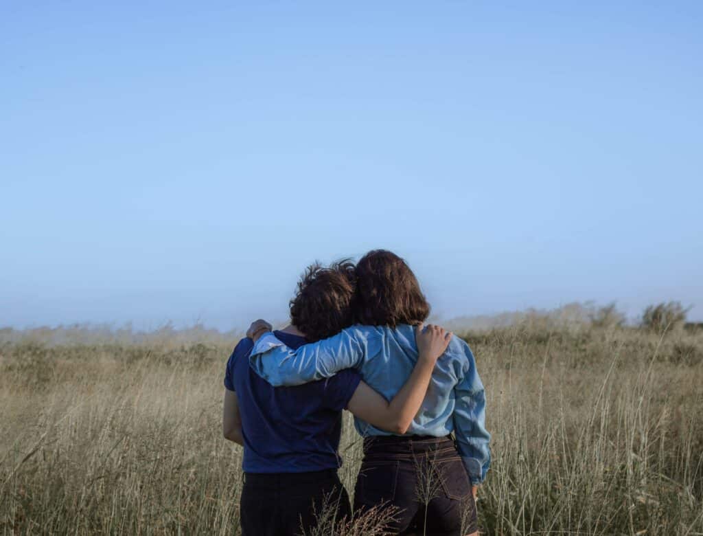 female friends embracing on spacious meadow