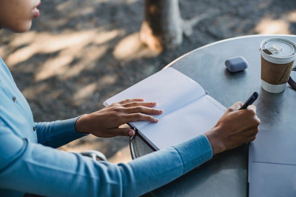 Photo of a Person in a Blue Top Writing on a Notebook